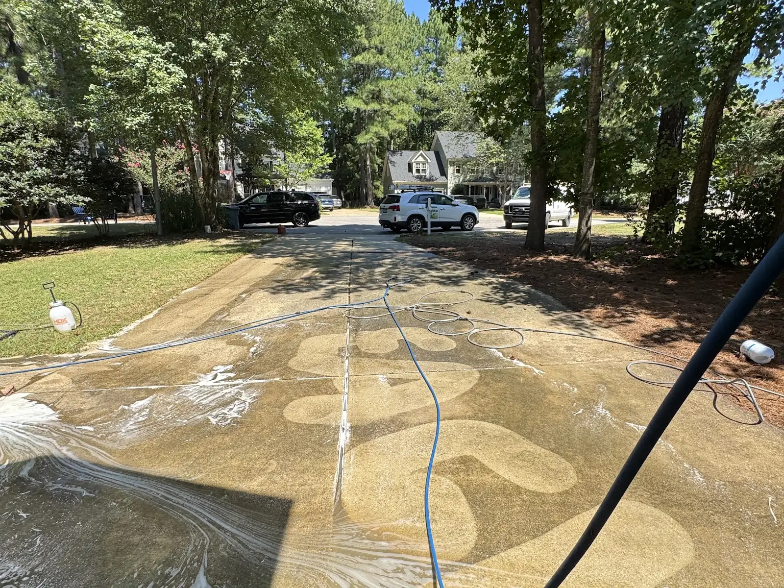 Pressure washing a concrete driveway in Apex NC showing red clay stain removal